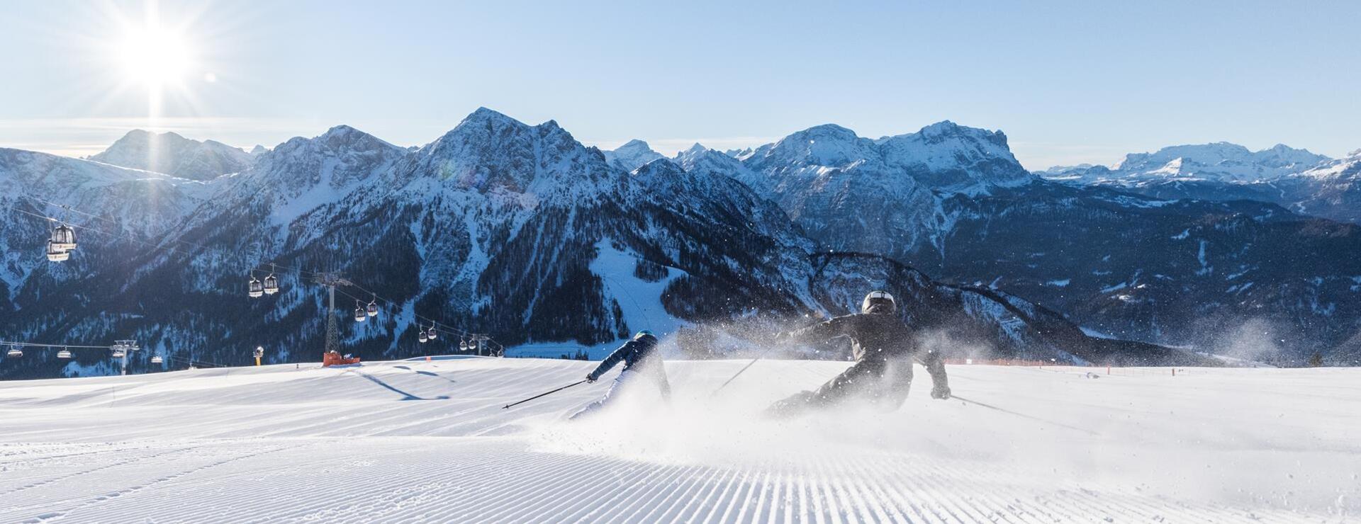 Zwei Skifahrer fahren eine Skipiste am Kronplatz bergab