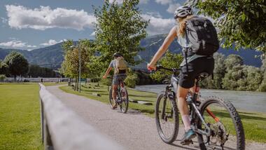 Two cyclists are riding along a path by the river